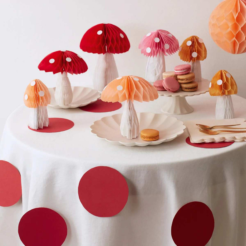 Centros de mesa de cogumelos de papel coloridos em mesa decorada com toalha branca e círculos vermelhos, com pratos e macarons.