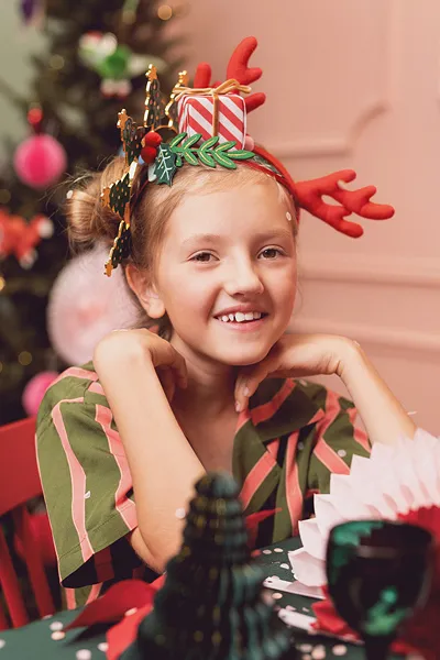 Menina com tiara de rena e decoração natalícia sentada à mesa