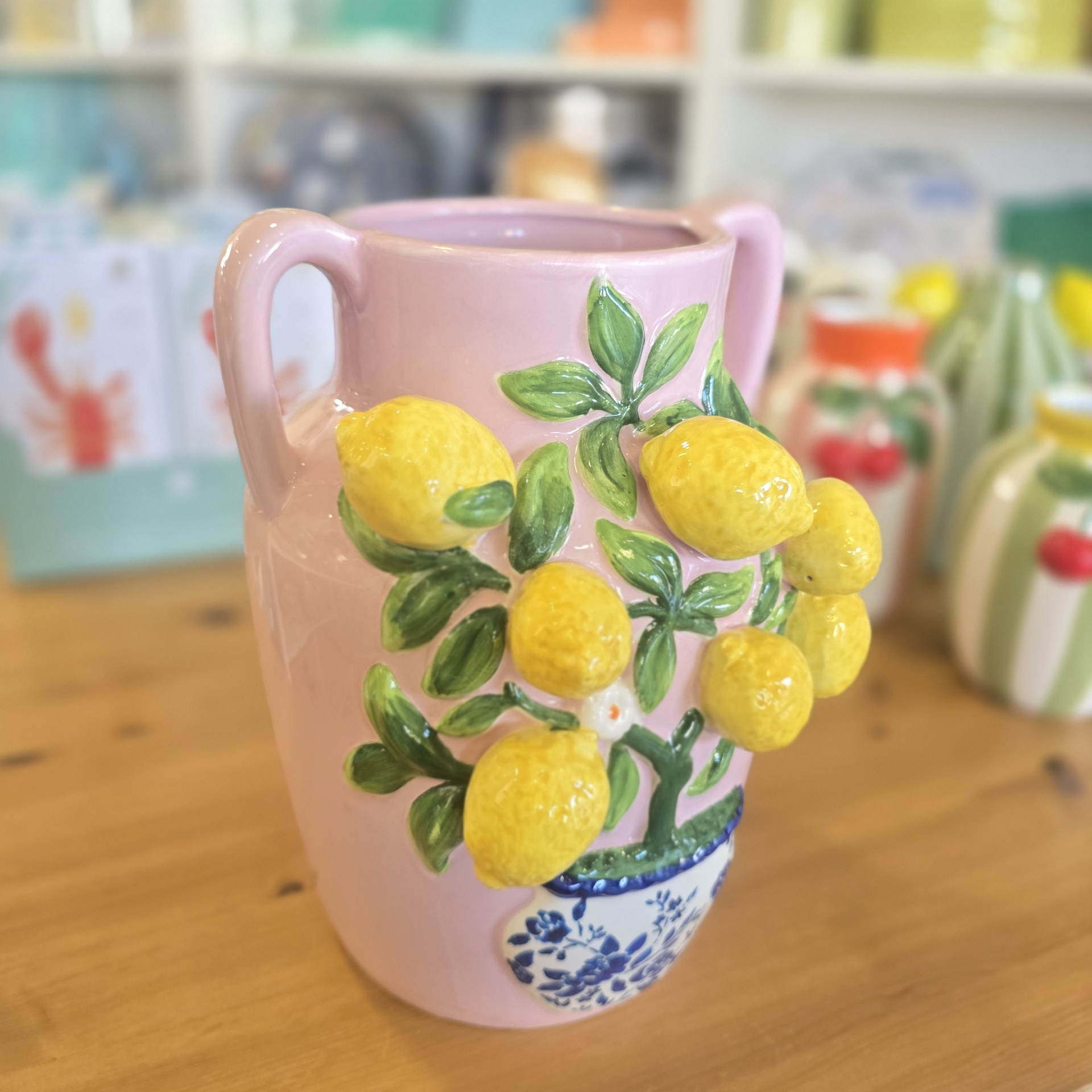 Jarro cerâmico cor-de-rosa decorado com limões em relevo sobre mesa de madeira