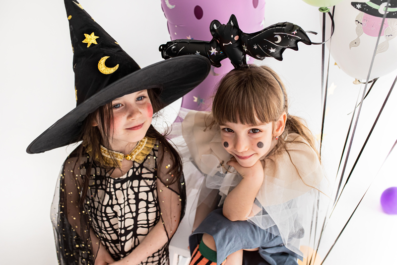 Duas crianças em roupas de Halloween com chapéu de bruxa e tiara de morcego