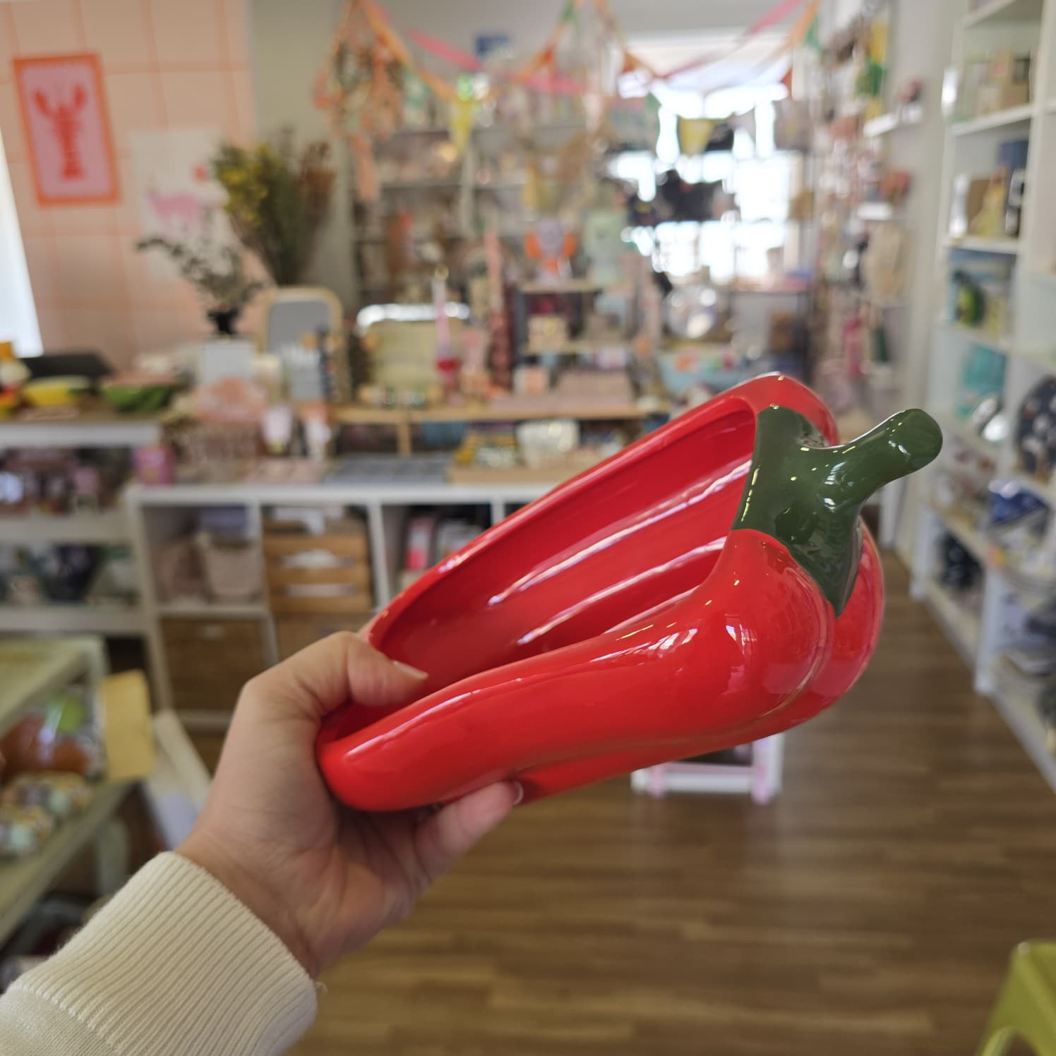 Prato cerâmico vermelho com formato de pimento, segurado por mão em loja