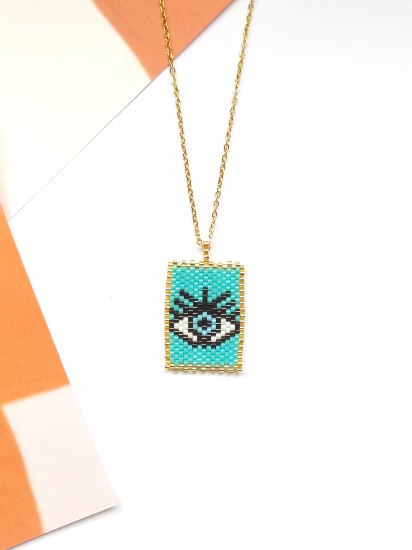 Colar dourado com pendente retangular colorido com padrão de olho