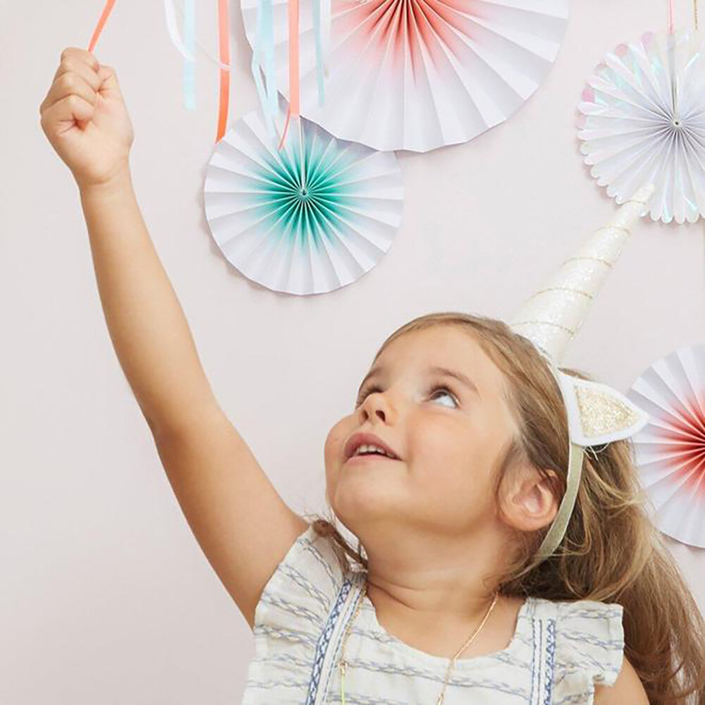 Menina com vestido claro e chapéu de unicórnio em fundo decorado com papel colorido