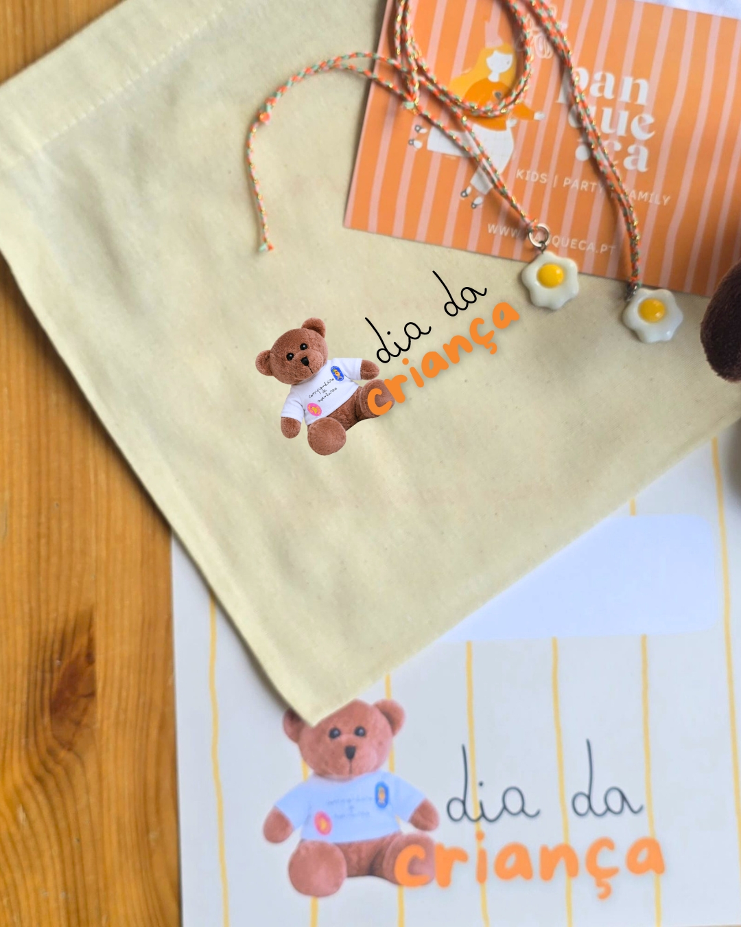 Saco de tecido bege com ursinho de peluche estampado e cartão laranja com colares de ovos estrelados