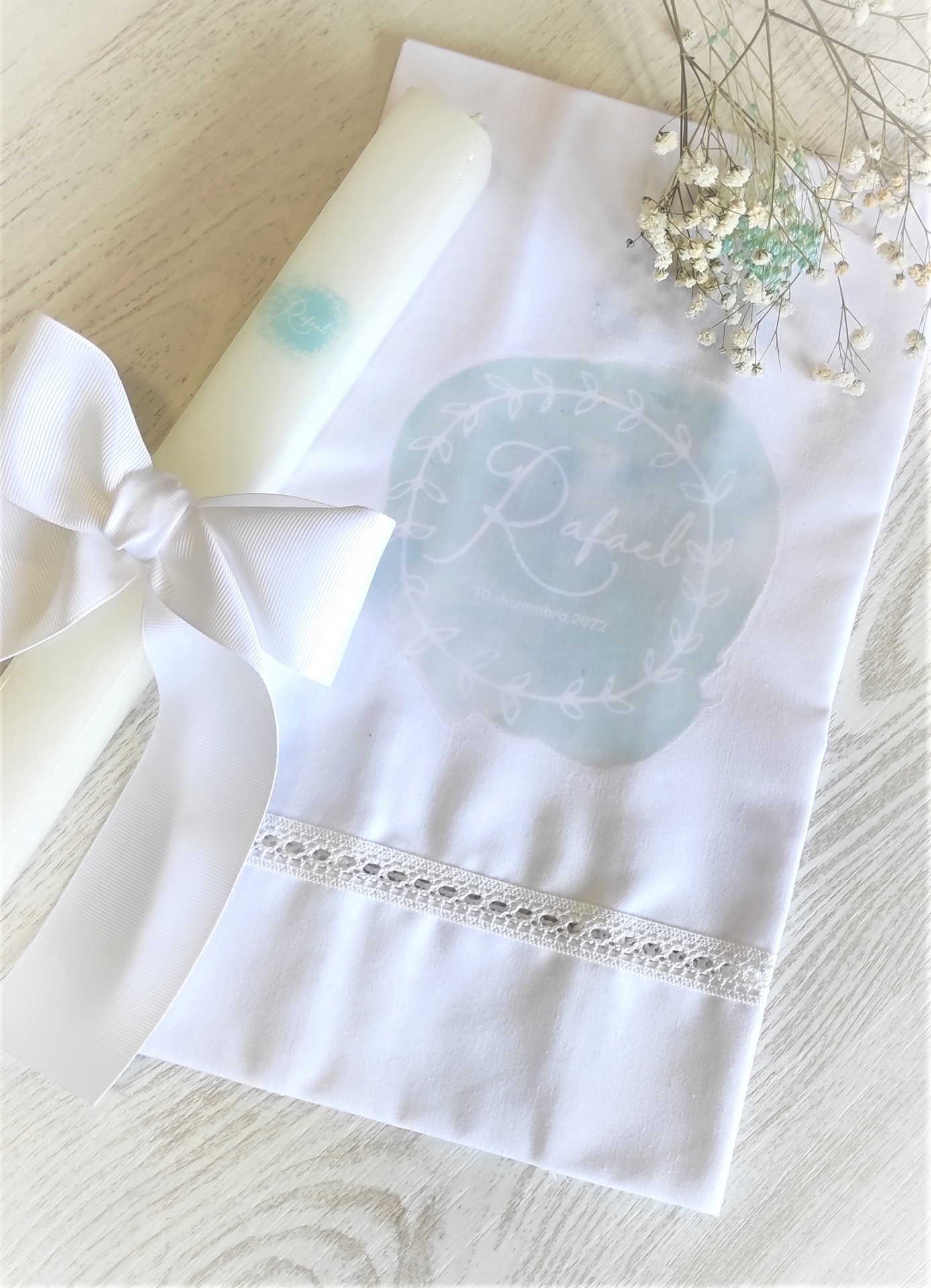 Vela branca com fita e toalha branca com padrão azul e nome Rafael