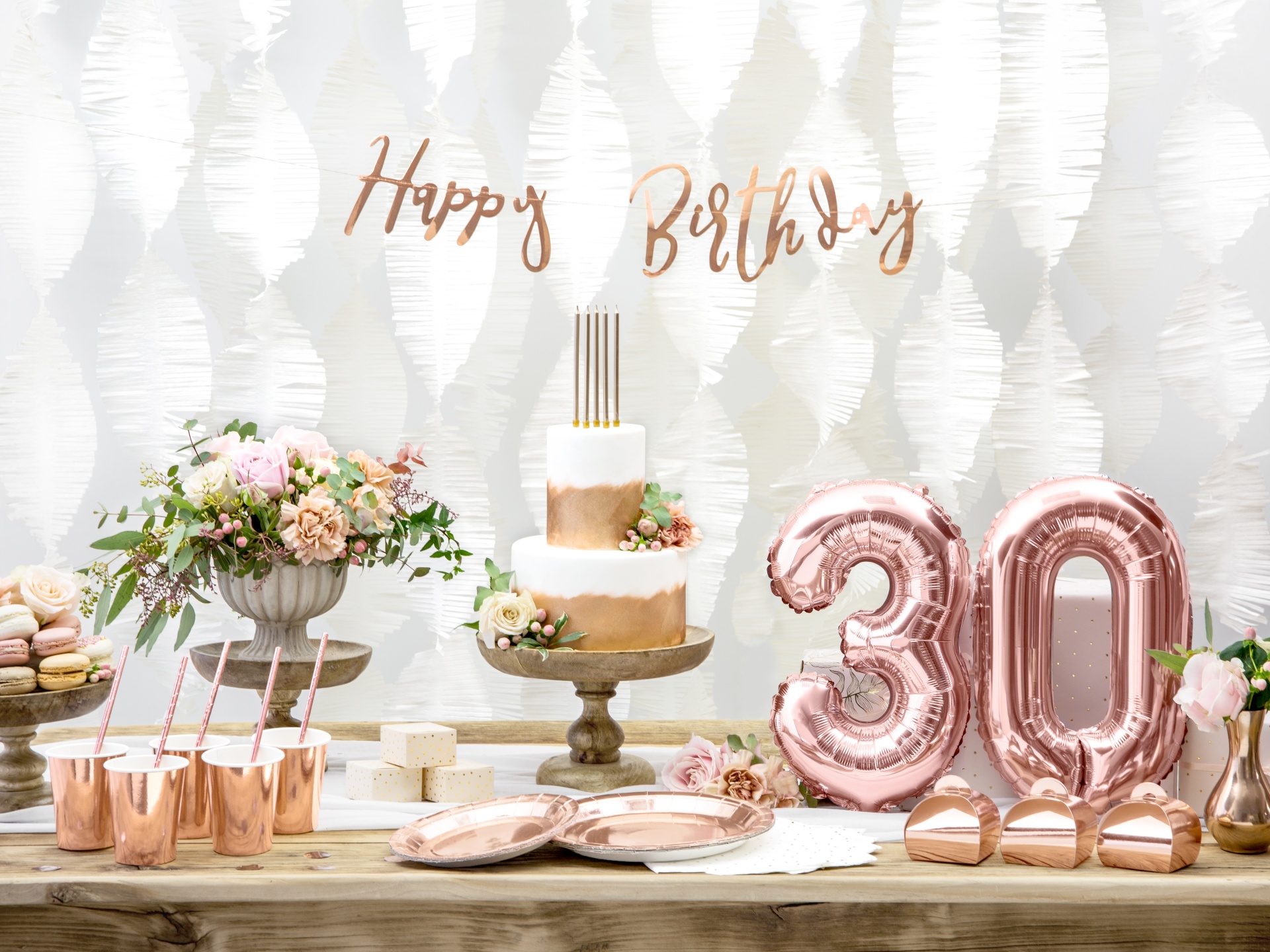 Mesa de festa com bolo branco e dourado, balões 30 rosa, flores, copos e decoração em tons rosa e dourado