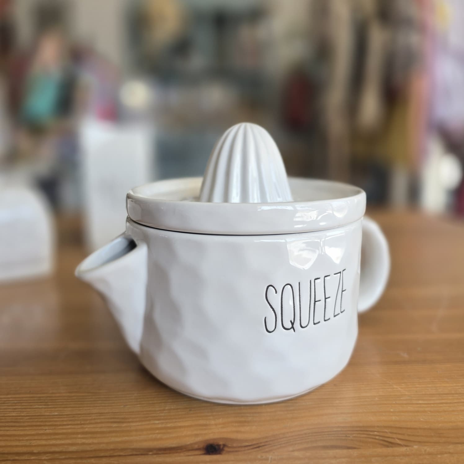 Espremedor de citrinos branco com texto SQUEEZE em mesa de madeira