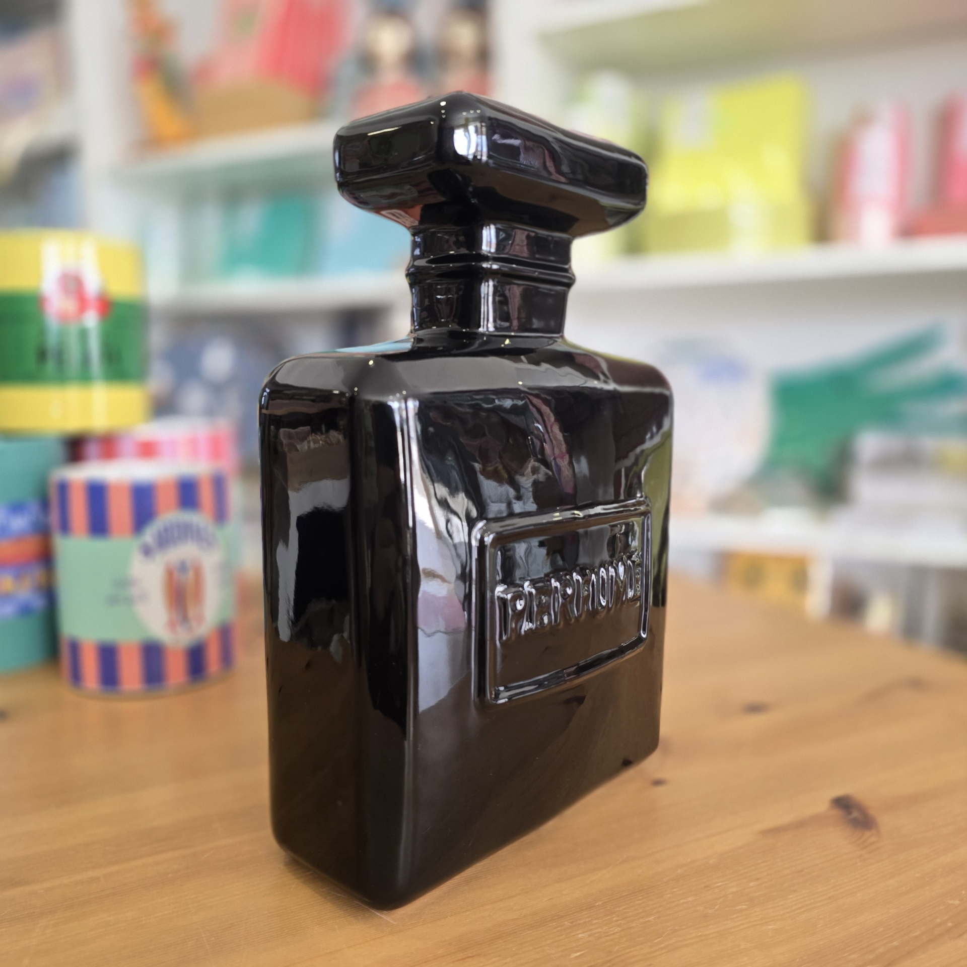 Frasco de perfume preto brilhante com relevo PERFUME em ambiente de loja.