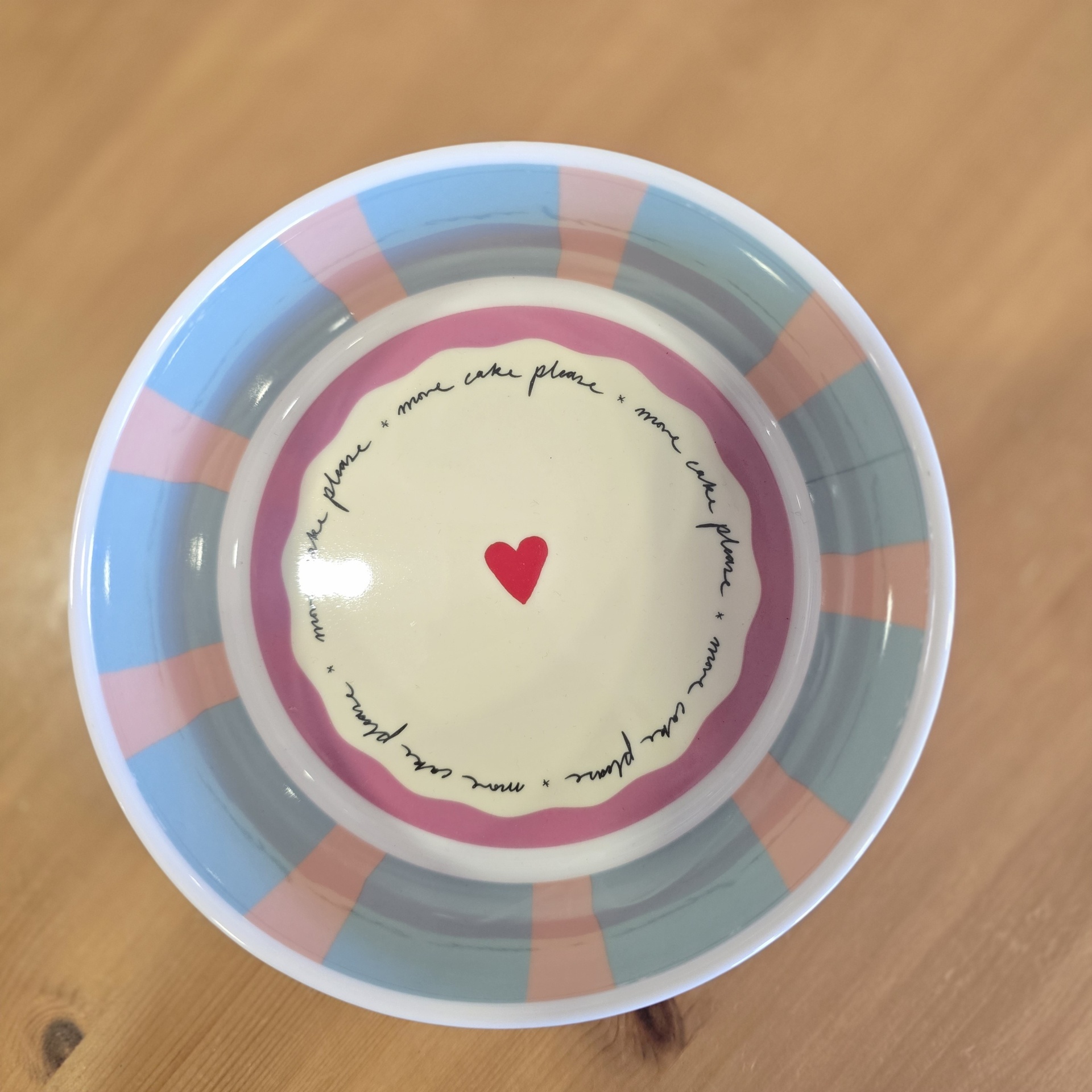 Prato cerâmico com padrão riscas azuis e rosas, texto repetido e coração vermelho no centro