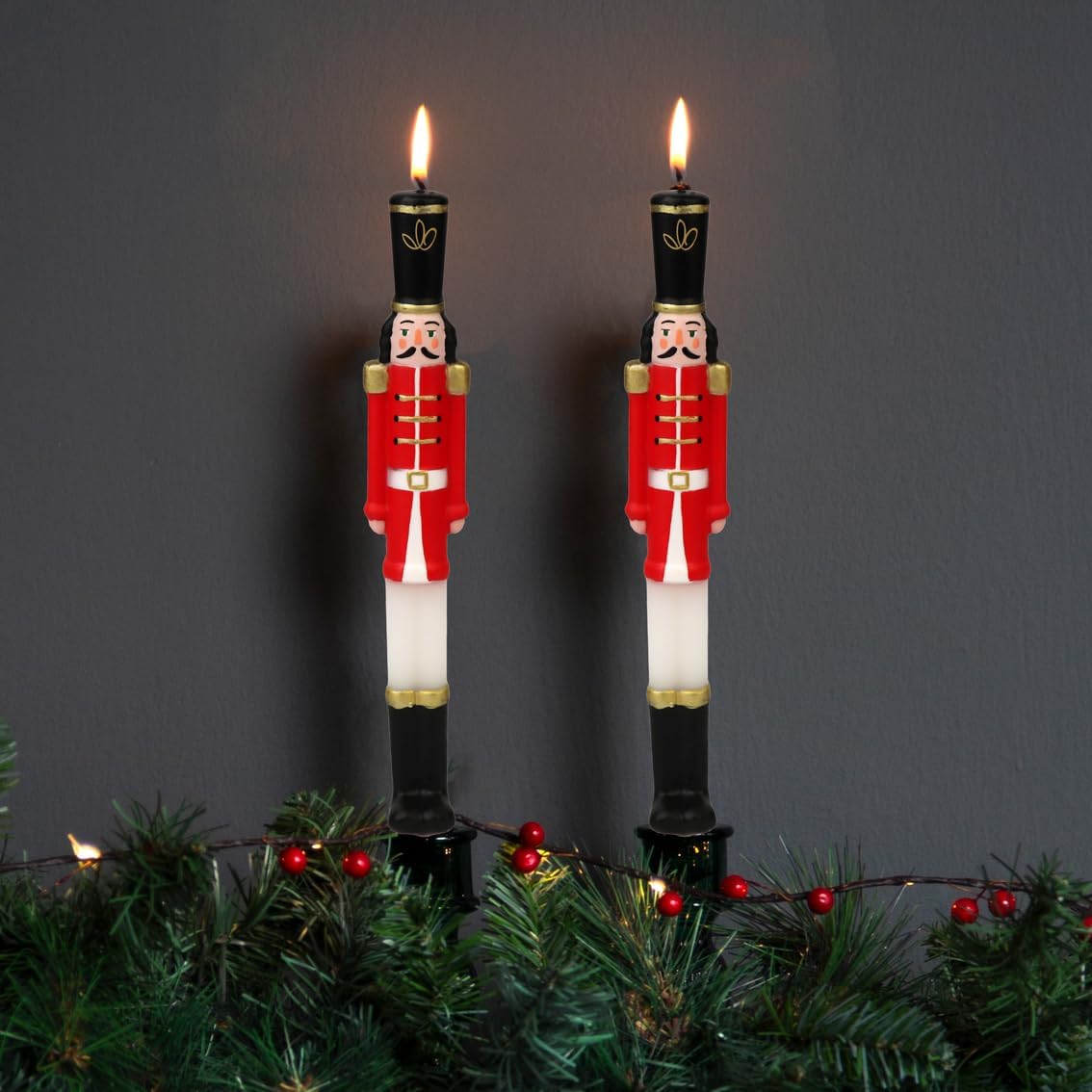 Velas decorativas de soldados do exército acesas em suporte preto com decoração verde e frutos vermelhos