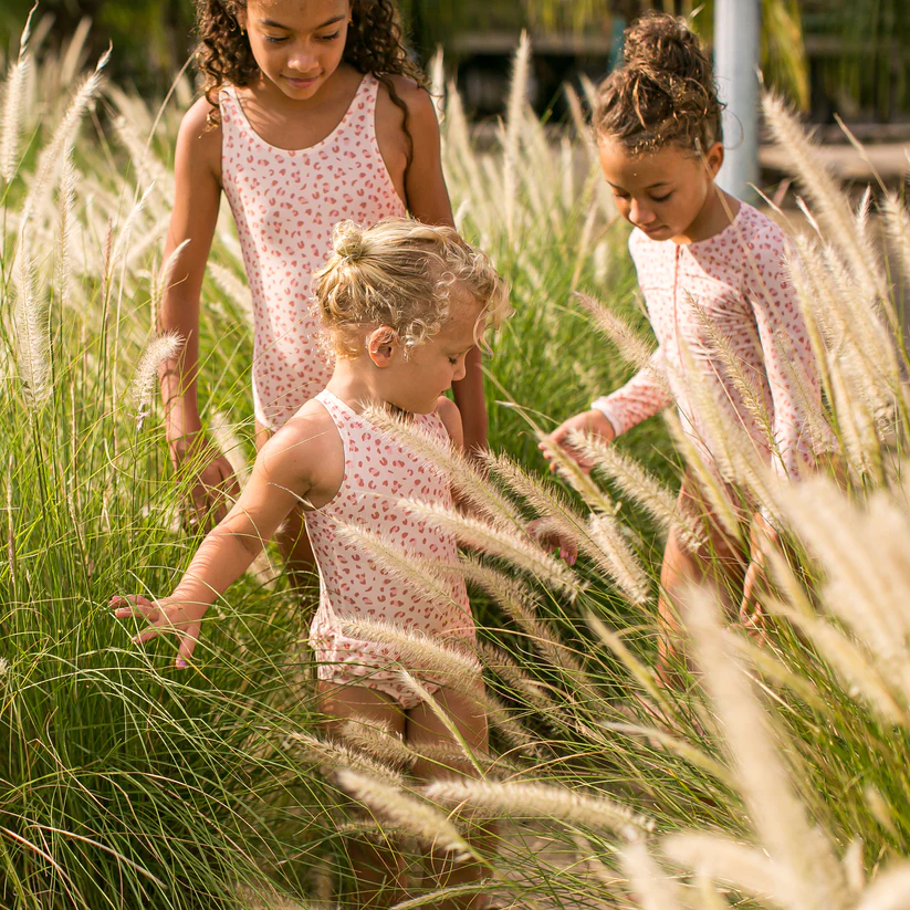 Três crianças com roupa interior floral em área com vegetação alta
