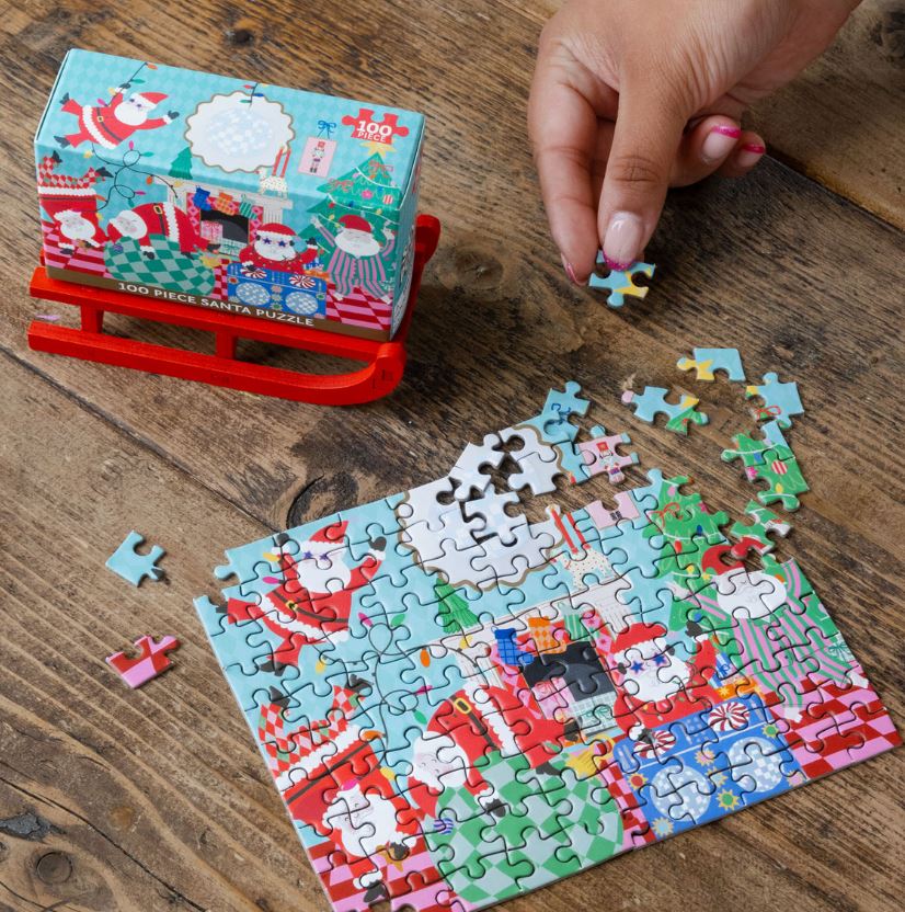 Puzzle de Natal com 100 peças, mostra Papai Noel, presentes coloridos, montado numa mesa de madeira