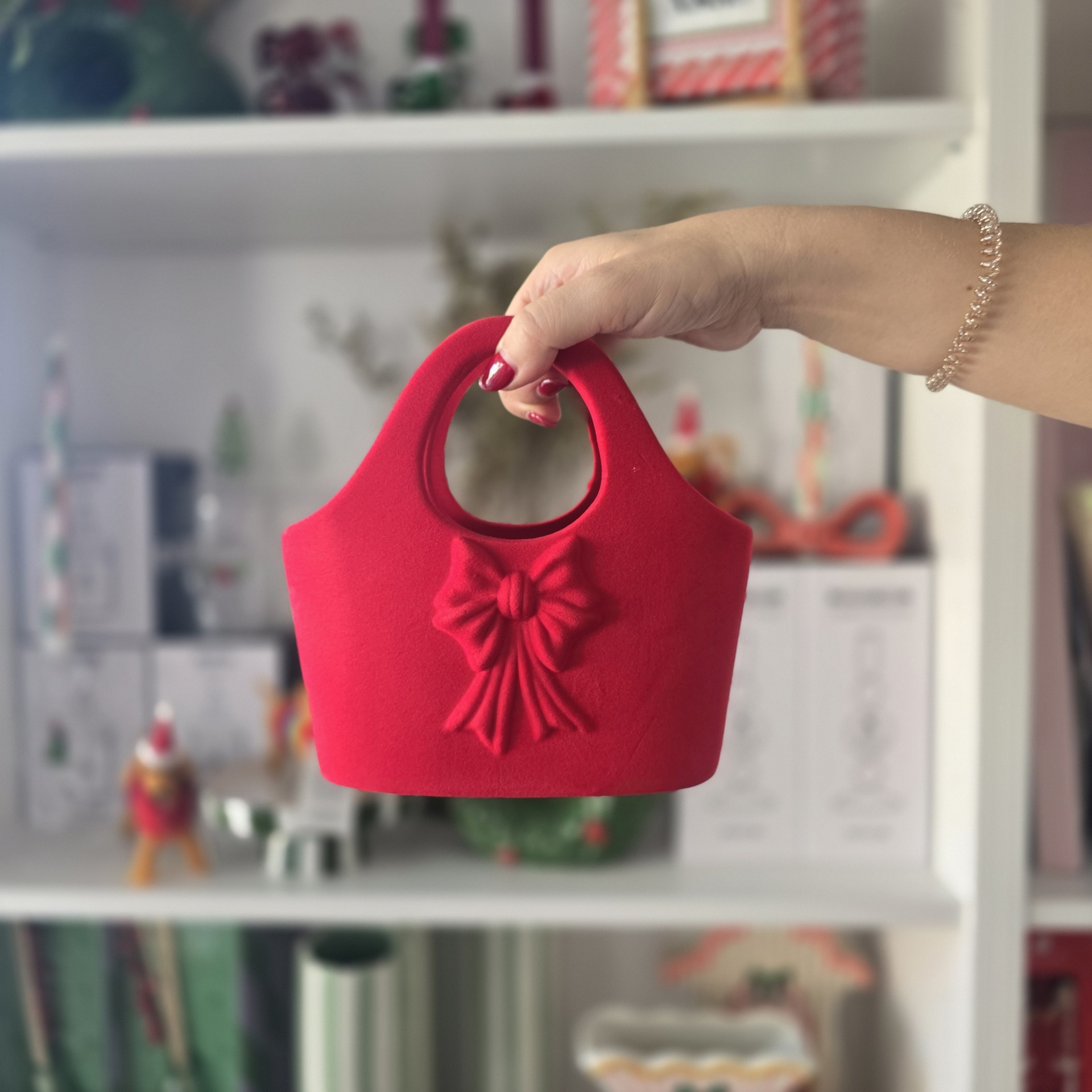Bolsa vermelha de feltro com laço sendo segurada por mão com pulseira
