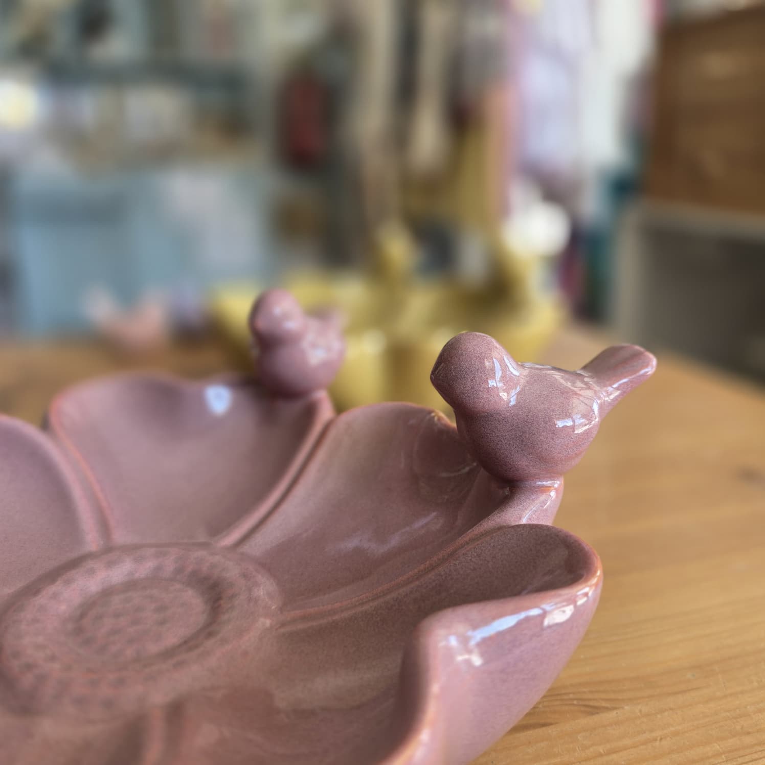 Prato decorativo cor de rosa em cerâmica com detalhes de pássaros nas bordas.