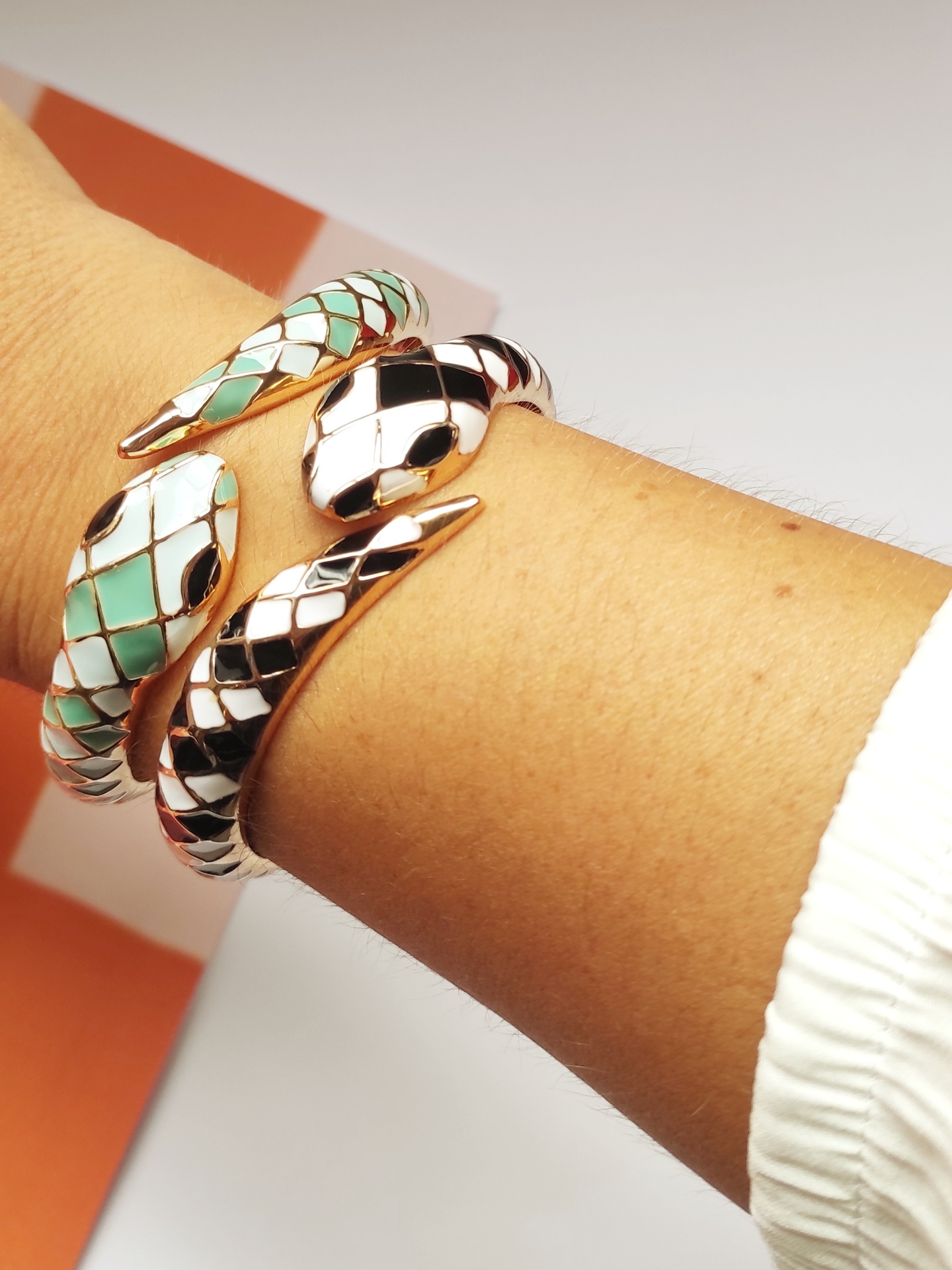 Pulseira dourada em forma de cobra com padrão de escamas coloridas no pulso