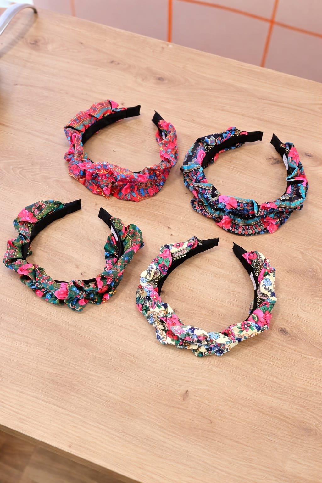 Cinco tiaras com padrões florais coloridos numa mesa de madeira clara