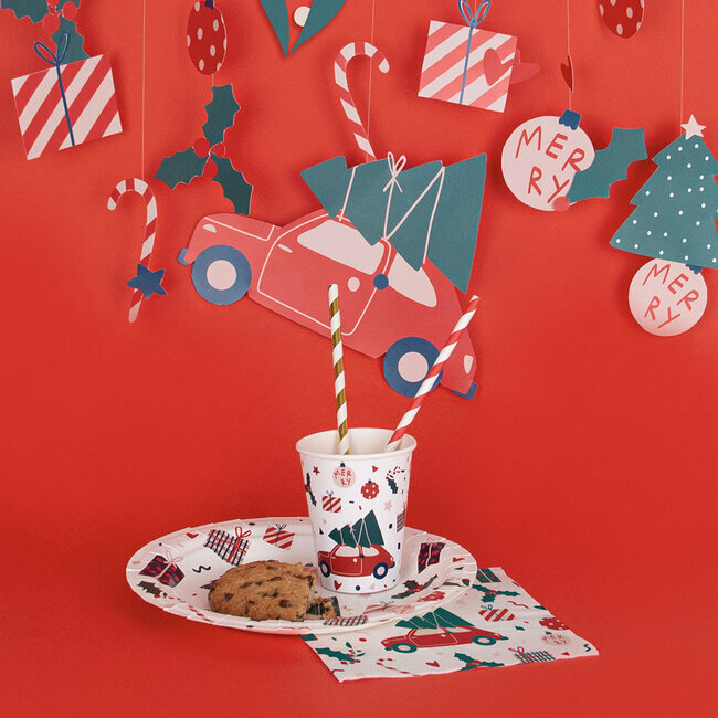 cenário natalício com copo, prato, guardanapo decorados, biscoito e decoração suspensa em fundo vermelho