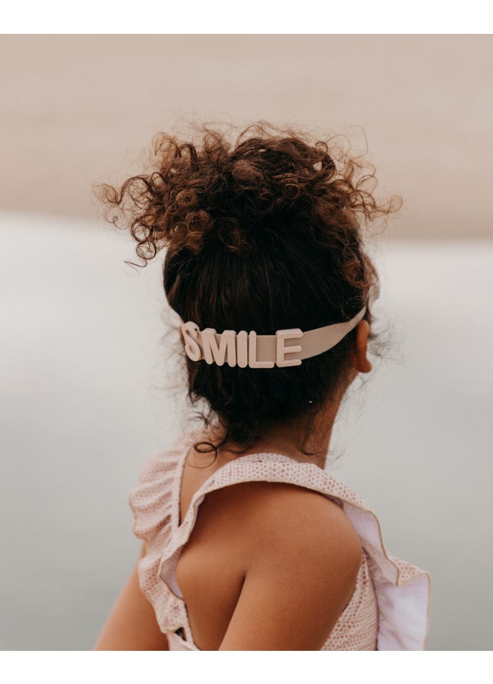 Criança com fita branca SMILE no cabelo e vestido cor-de-rosa claro vista de costas
