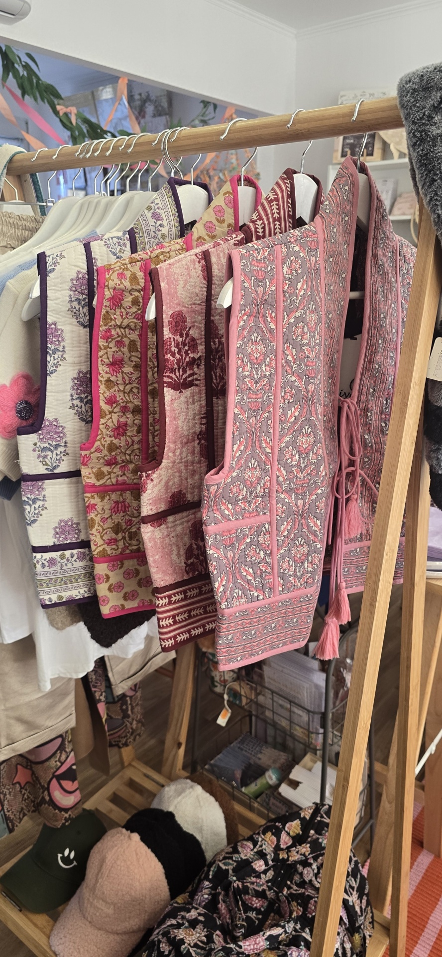 Coleção de coletes florais em tons rosa e vinho pendurados em estrutura de madeira