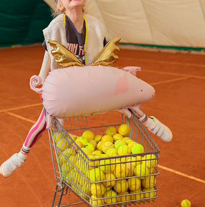 Carrinho com bolas de ténis e balão inflável em forma de porco com asas