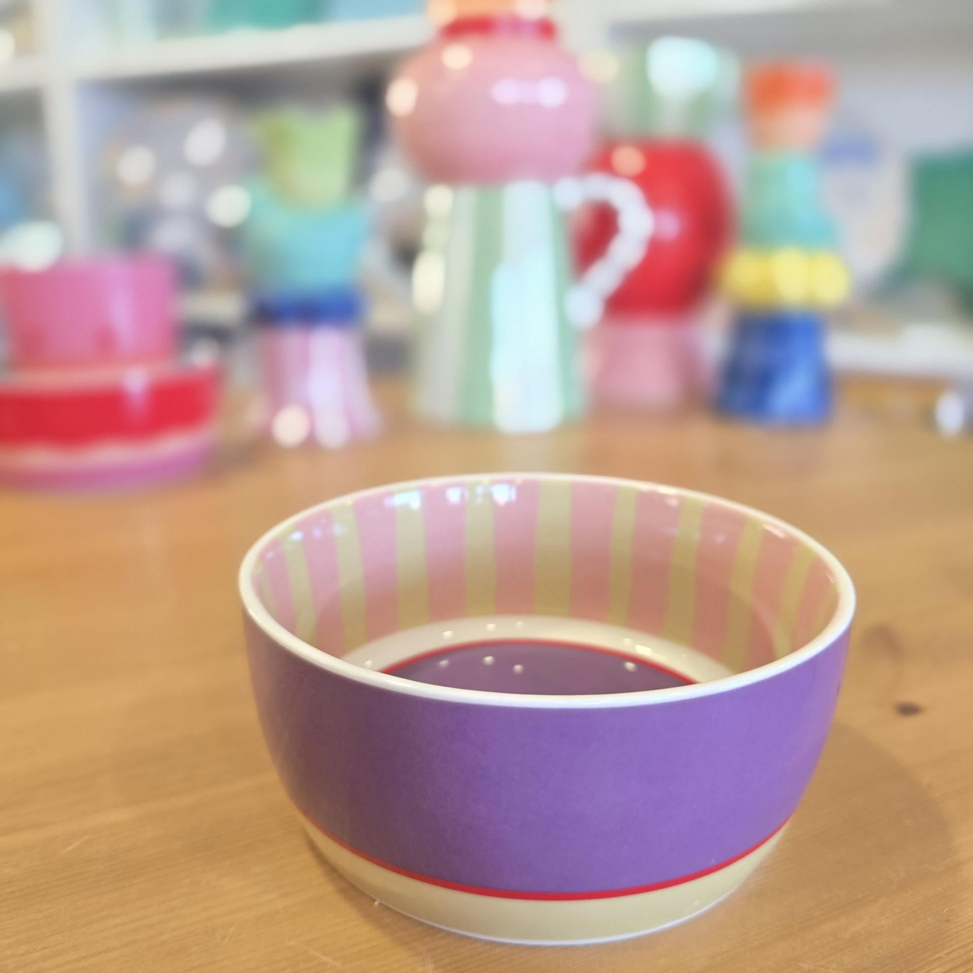 Tigela cerâmica roxa com riscas amarelas e rosa no interior sobre mesa de madeira.