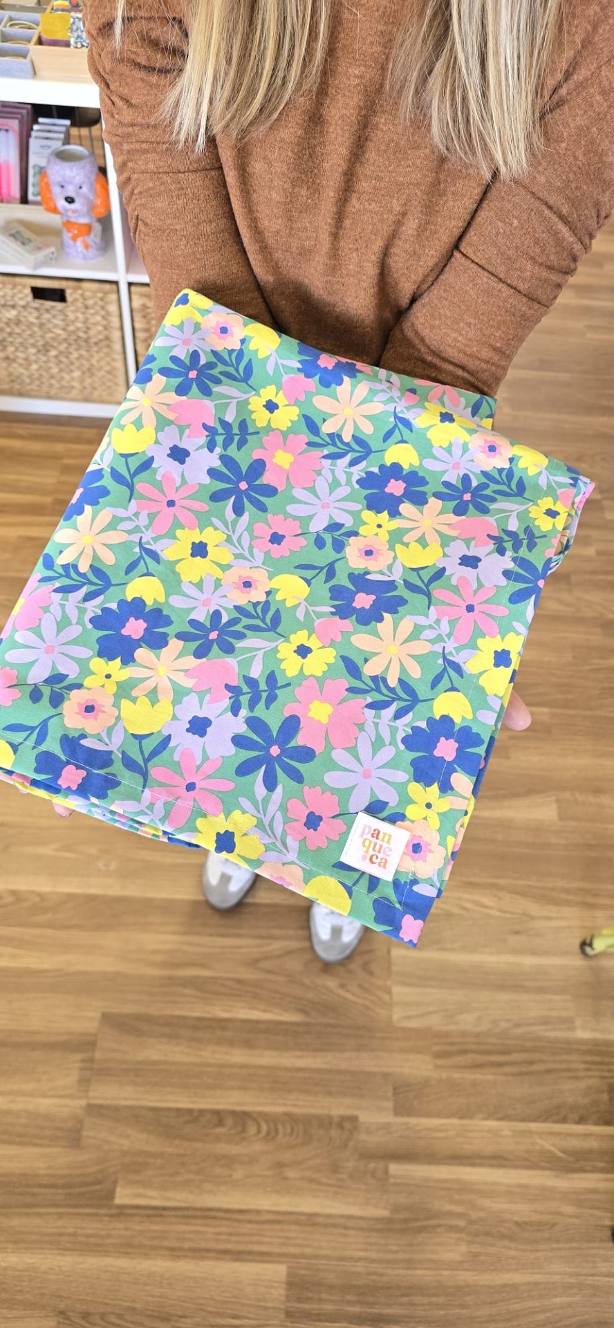 Tecido floral multicolorido sendo segurado por pessoa de casaco castanho em piso de madeira