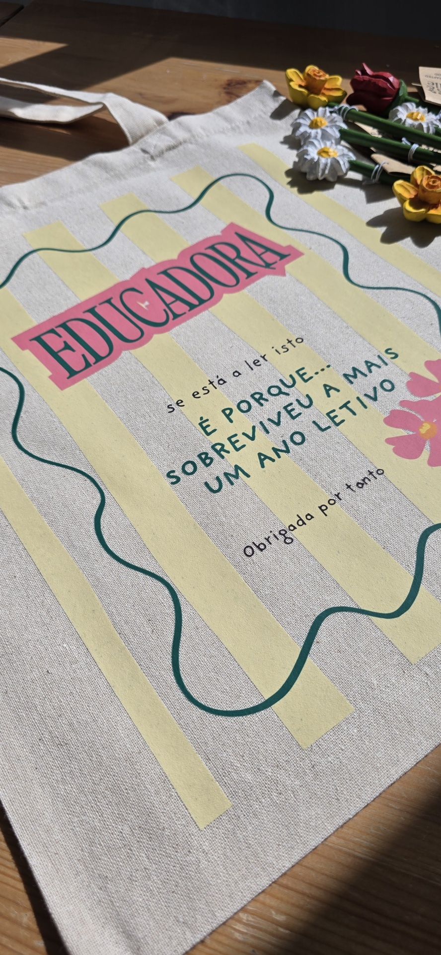 Saco de tecido com texto e flores decorativas sobre superfície de madeira