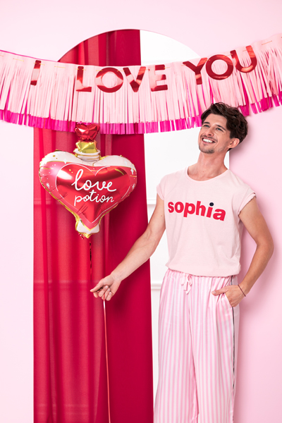 Homem com t-shirt 'sophia' e calças riscas cor-de-rosa com balão 'love potion' e decoração 'I LOVE YOU'
