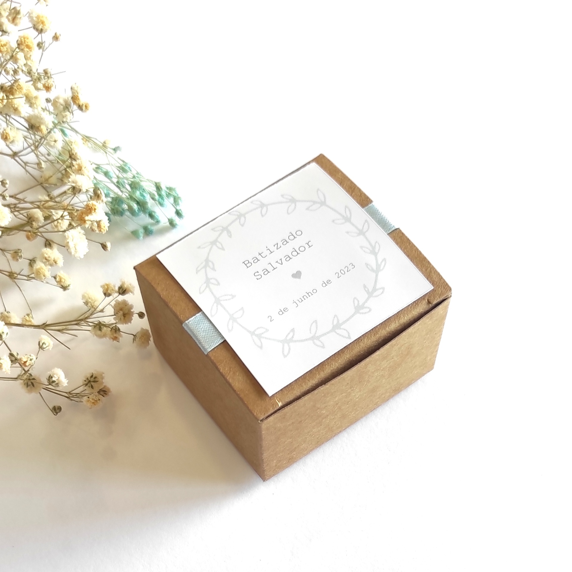Caixa de batizado castanha com etiqueta branca e flores secas