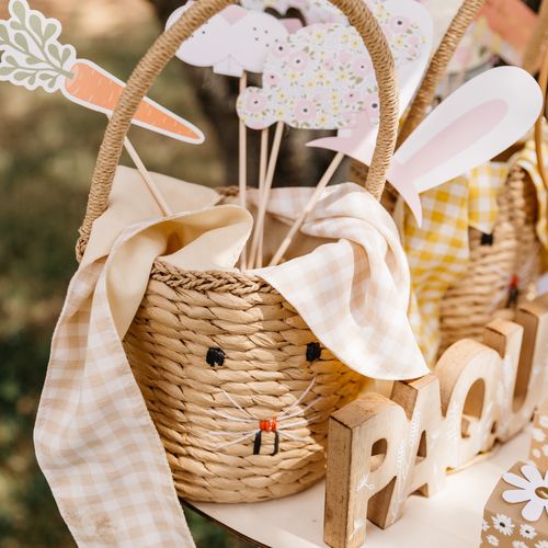 Cesto de palha decorado como coelho com acessórios de papel e pano xadrez.