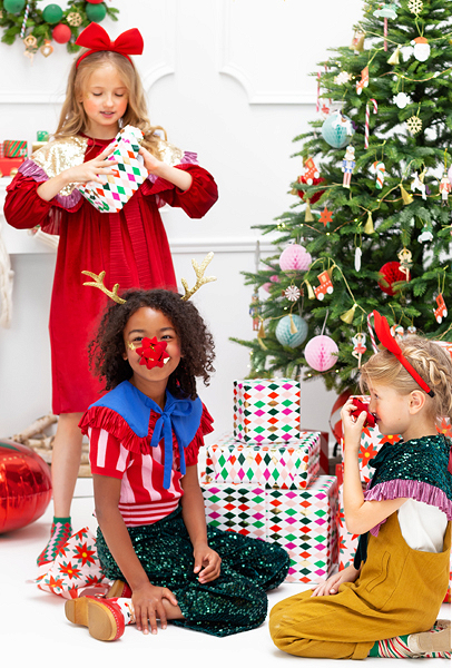 Crianças vestidas para Natal ao lado de árvore e presentes coloridos