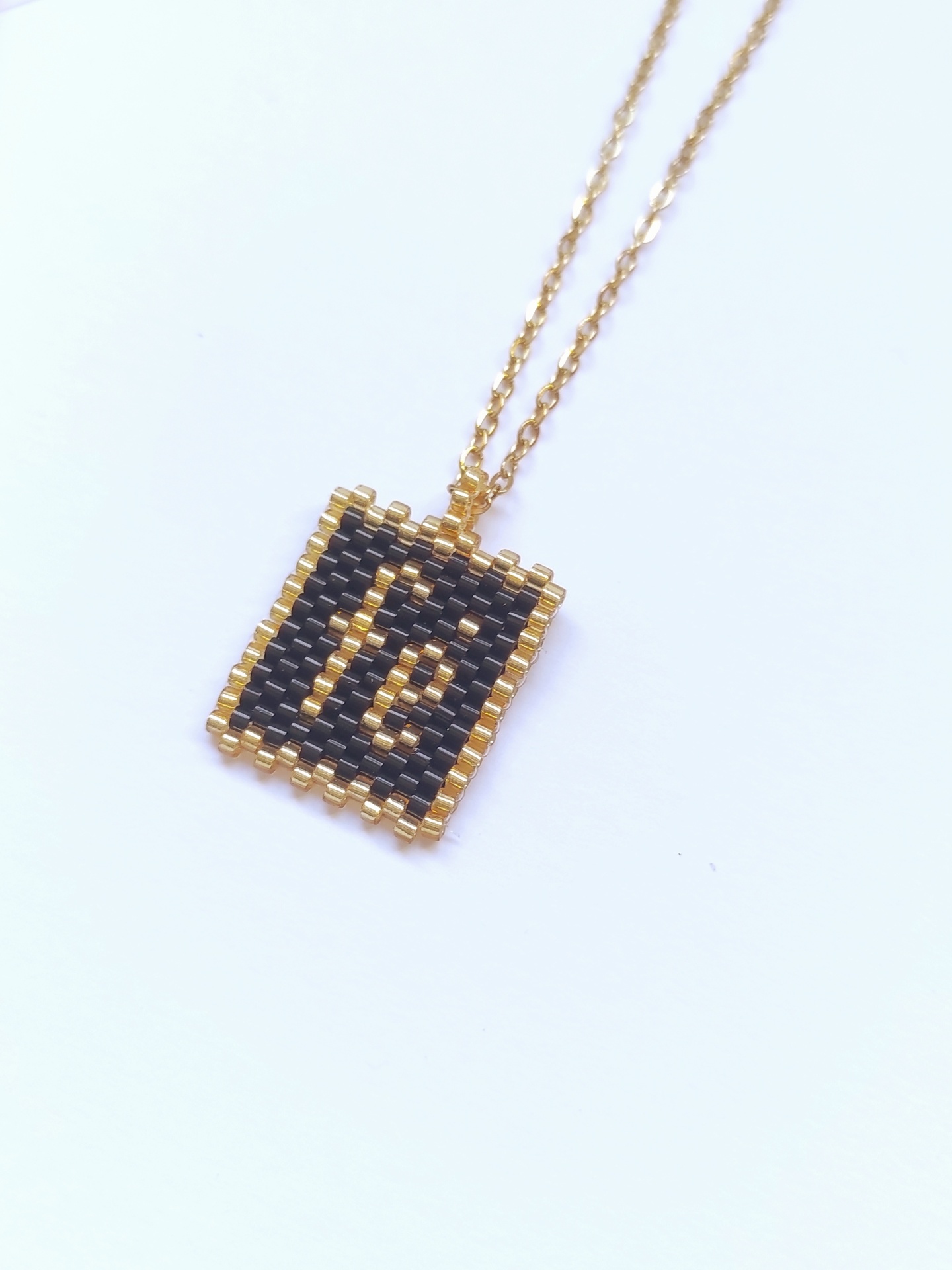 Colar com pendente quadrado em contas pretas e douradas com palavra 'fé'
