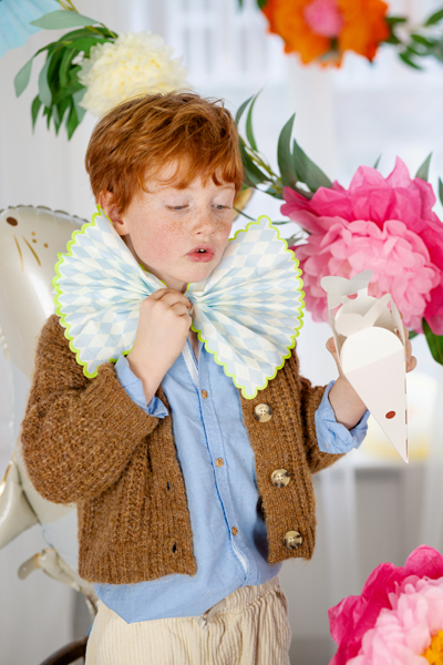 Criança ruiva com acessório de papel e laço em ambiente decorado com flores e balão