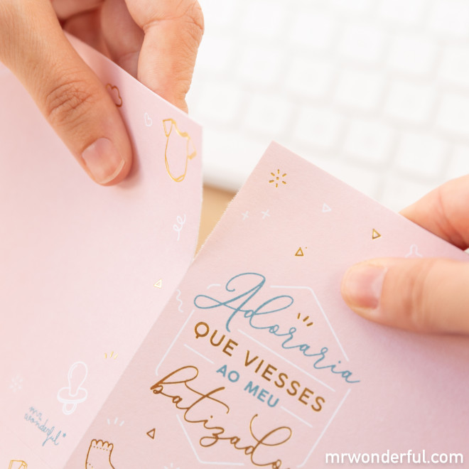 Cartão de batizado rosa claro com texto em azul e dourado e ilustrações, mãos segurando, teclado ao fundo