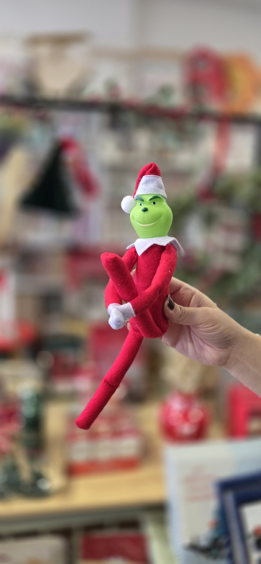 Boneco Grinch de pelúcia com chapéu de Natal sendo segurado