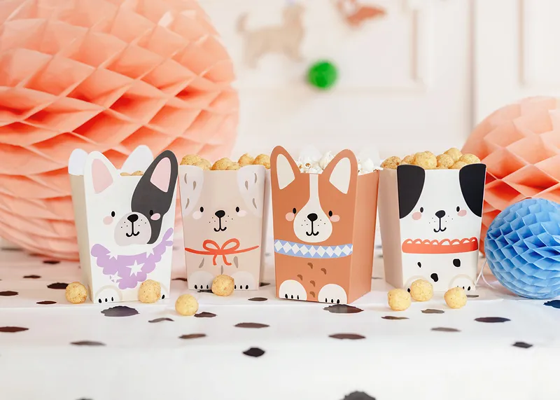 Caixas de papelão com desenhos de cães contendo pipoca numa mesa decorada com confetes e adornos de papel