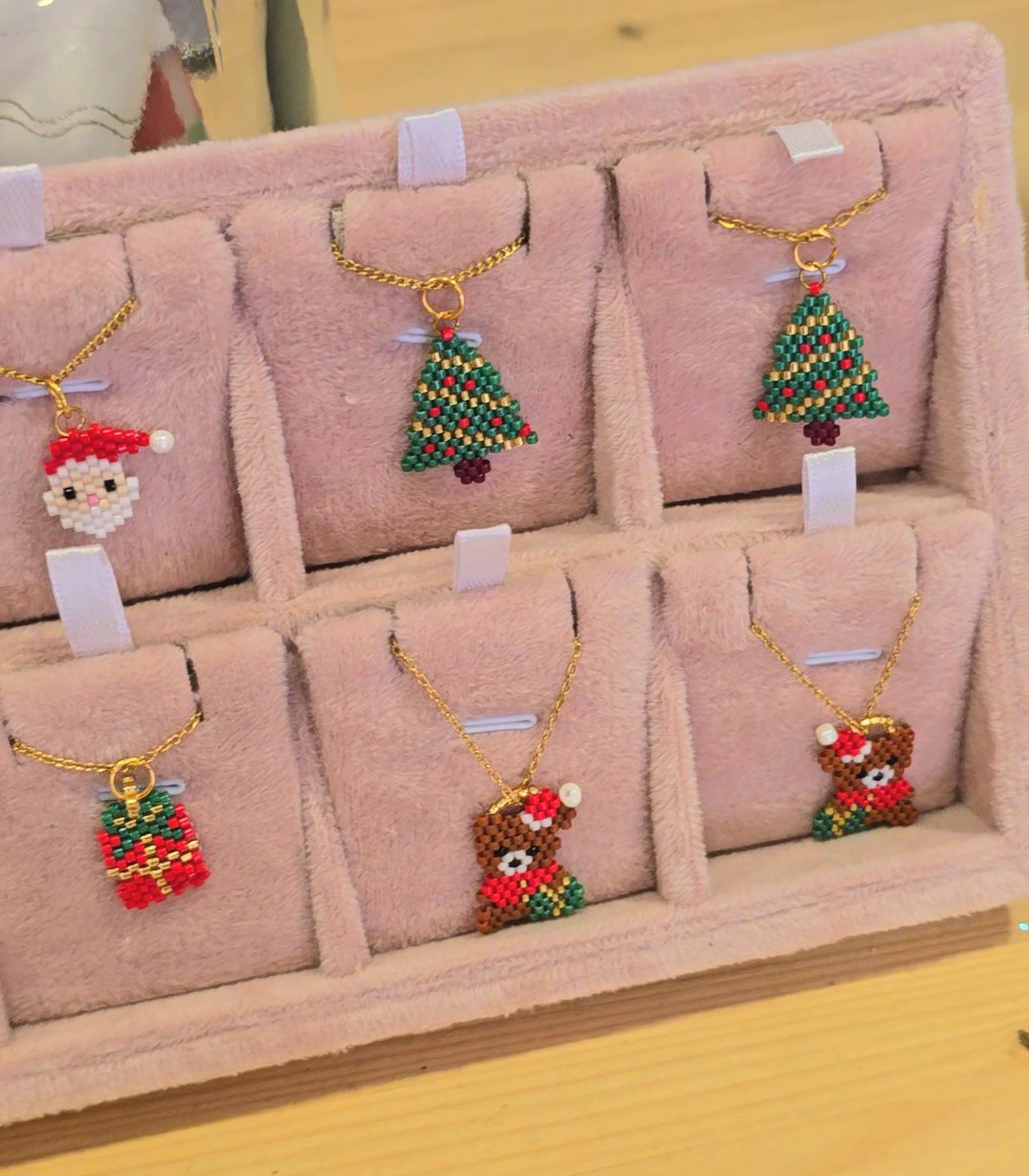 Colares com pendentes de contas em forma de Pai Natal, árvore de Natal, prenda e urso, exposição em almofada rosa.