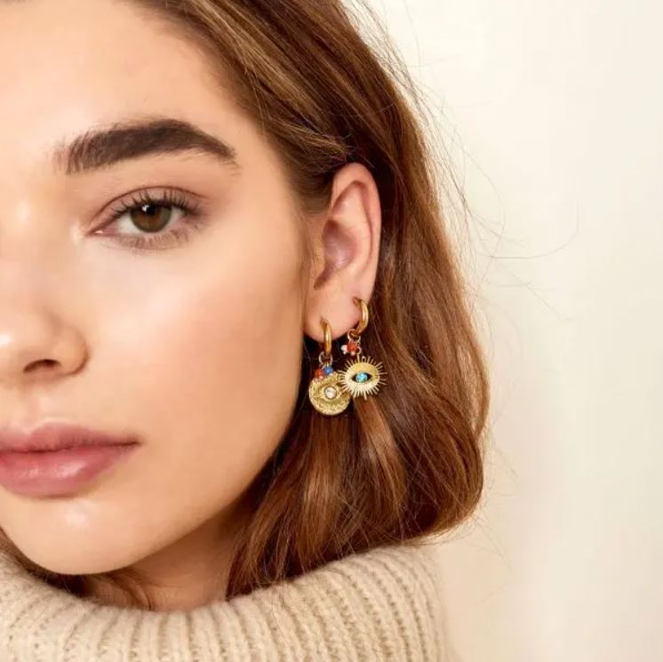 Brincos dourados com olhos decorativos em mulher com suéter bege