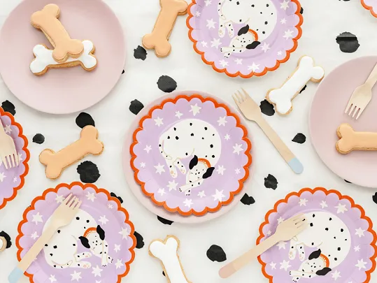 Pratos descartáveis decorados com dálmatas, ossos e talheres de madeira sobre fundo branco com manchas pretas