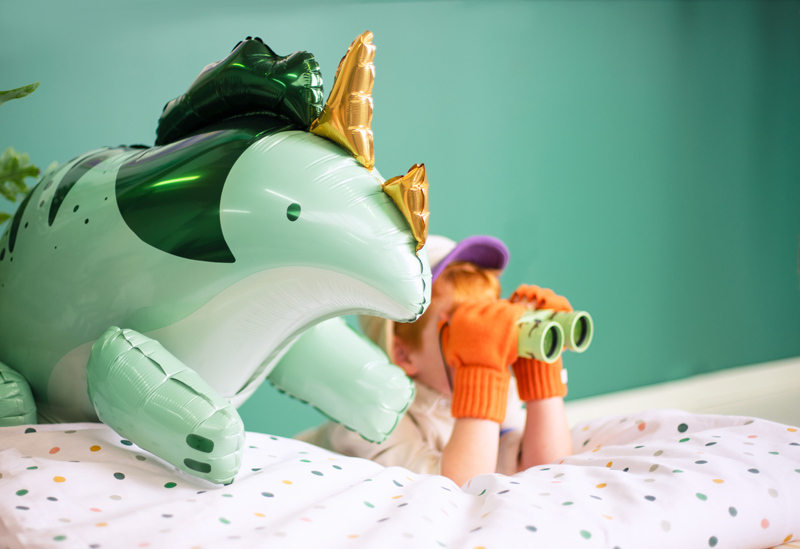 Balão insuflável dinossauro sobre cama com crianças ao fundo