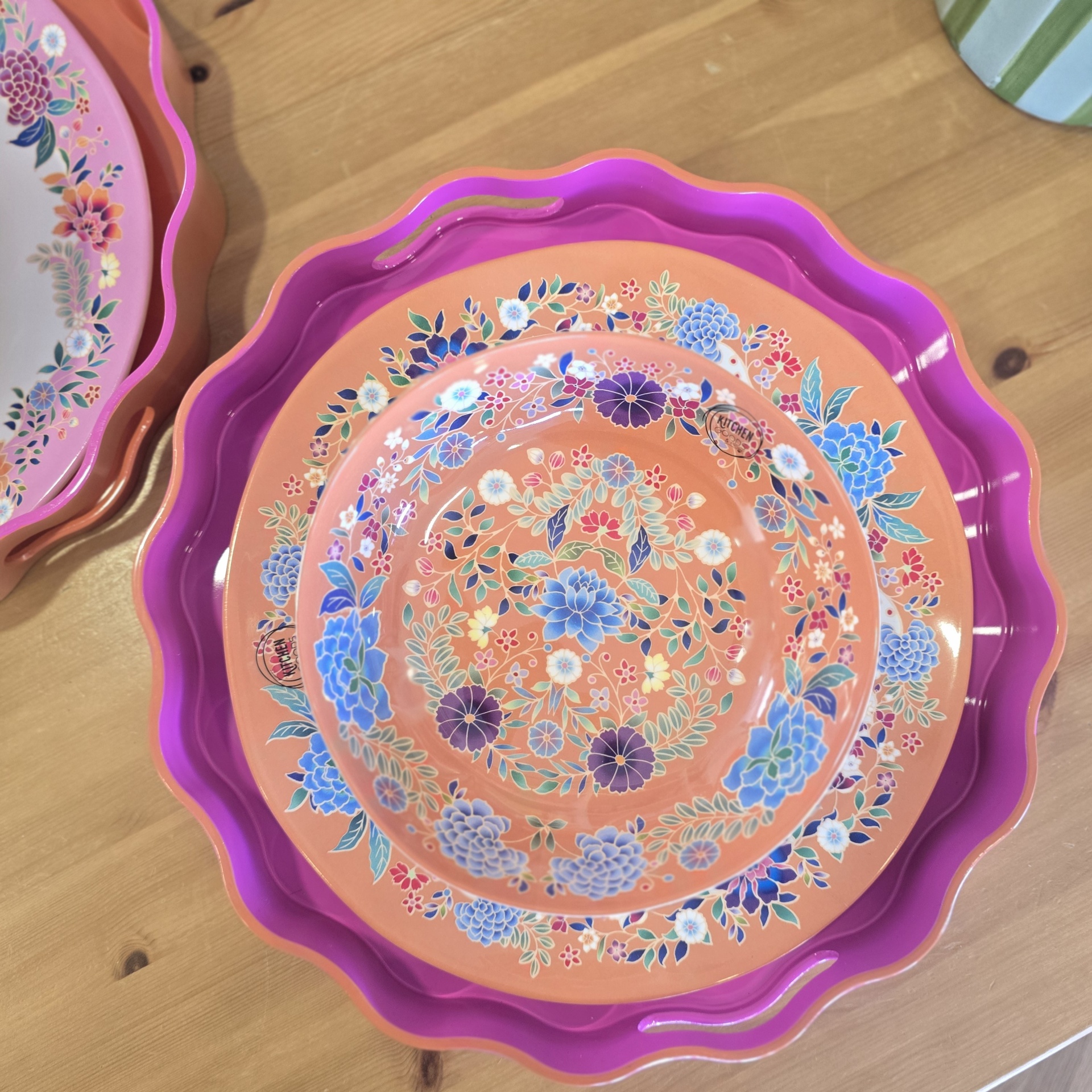 Três tabuleiros de plástico com padrão floral em rosa e lilás sobre mesa de madeira