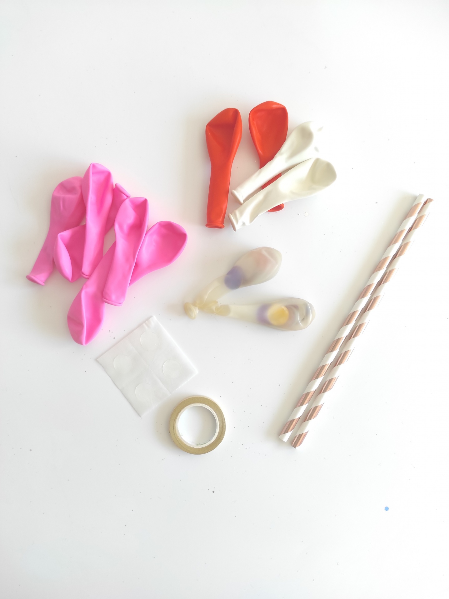 balões coloridos, canudos de papel, fita adesiva e adesivos pequenos numa superfície branca