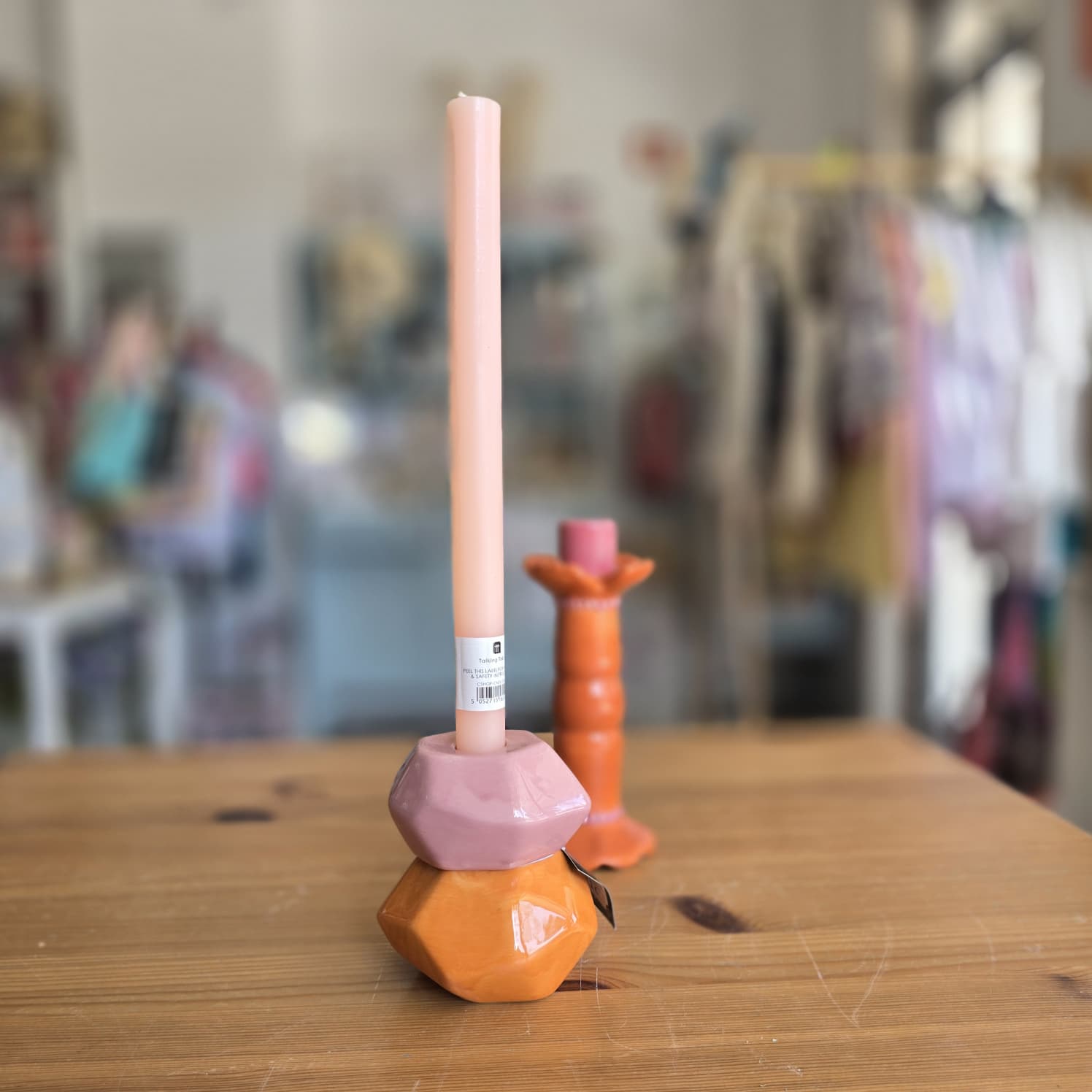 Vela rosa clara alta num suporte cerâmico azul-petróleo e laranja sobre mesa de madeira