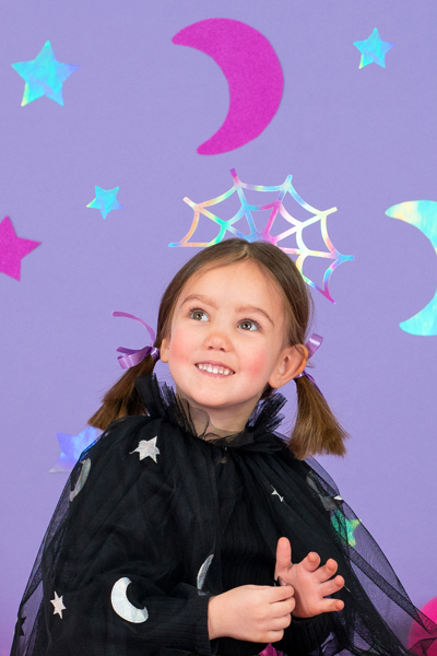 Criança com capa preta de estrelas e luas e acessório de cabeça prateado com padrão de teia