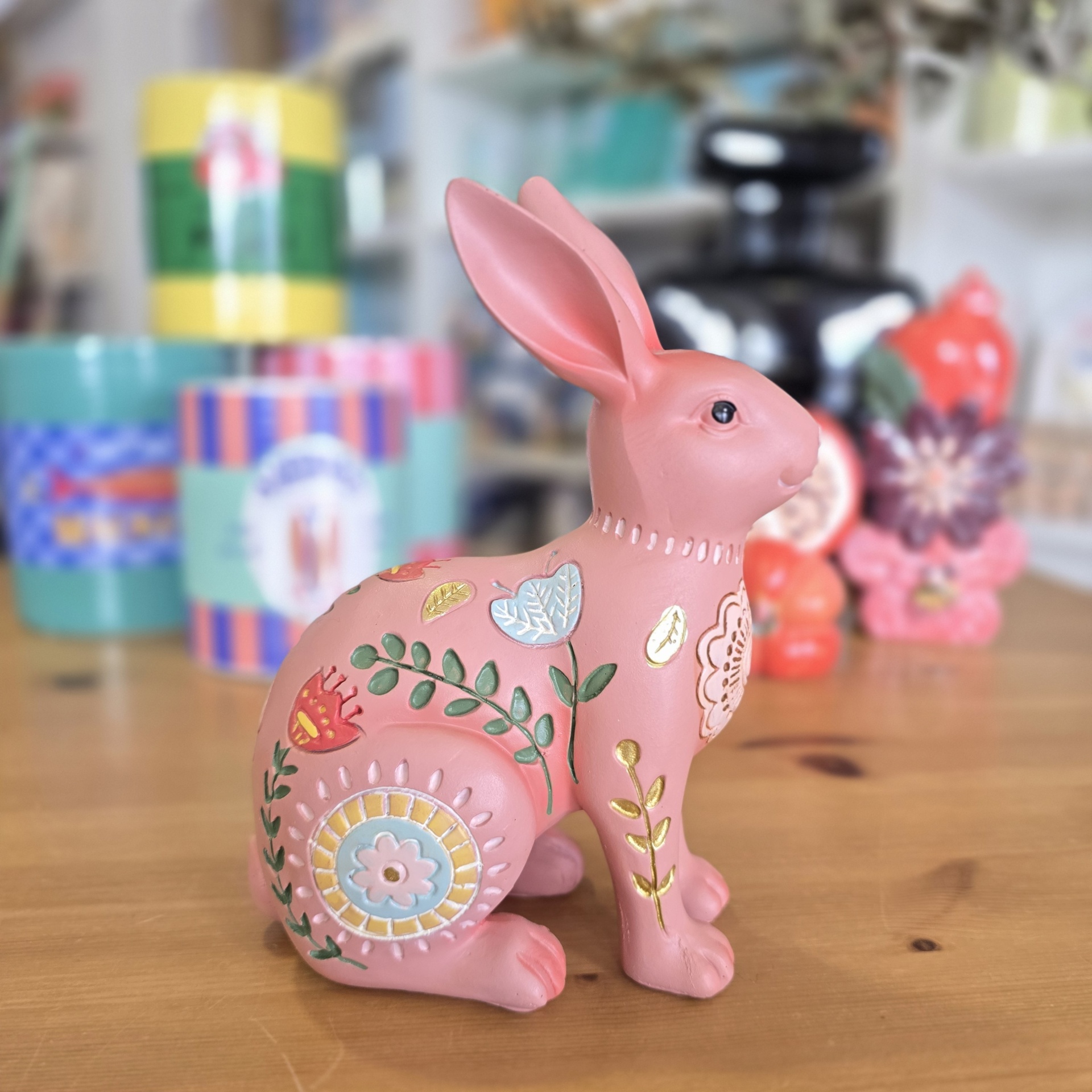 Figura decorativa de coelho rosa com padrões florais sobre mesa de madeira