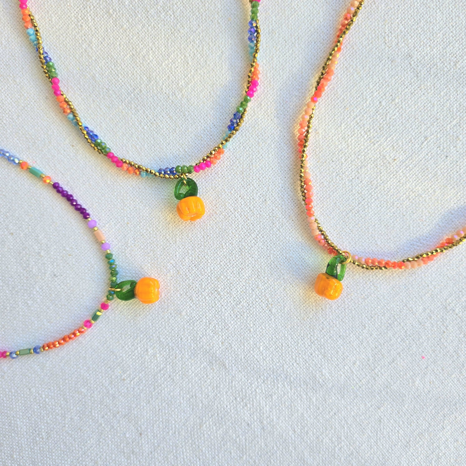 Três colares de contas coloridas com pendente de abóbora laranja em fundo branco