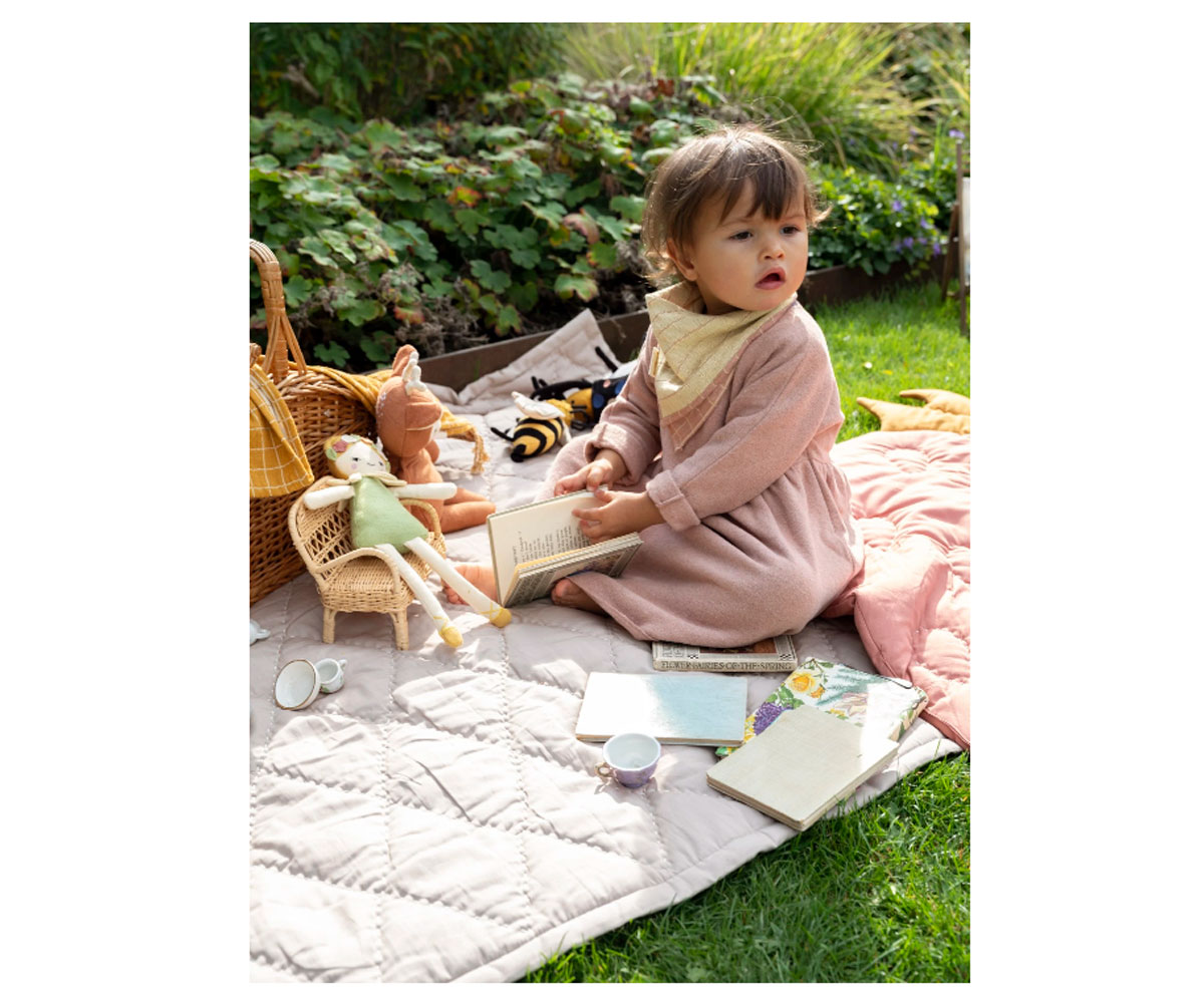 Bebé sentado numa manta acolchoada com bonecas de pano e brinquedos em relva