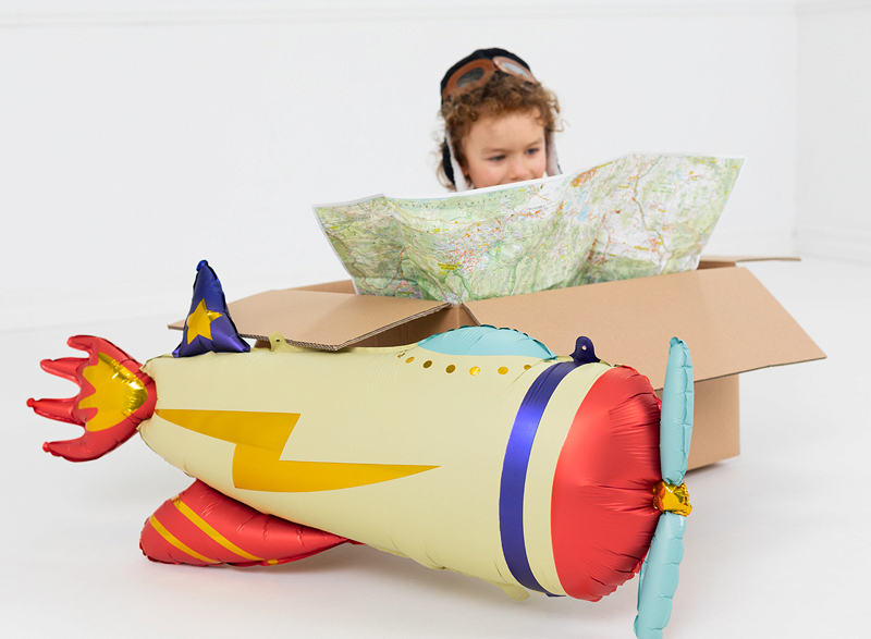 Criança segurando mapa dentro de caixa ao lado de balão em forma de avião colorido