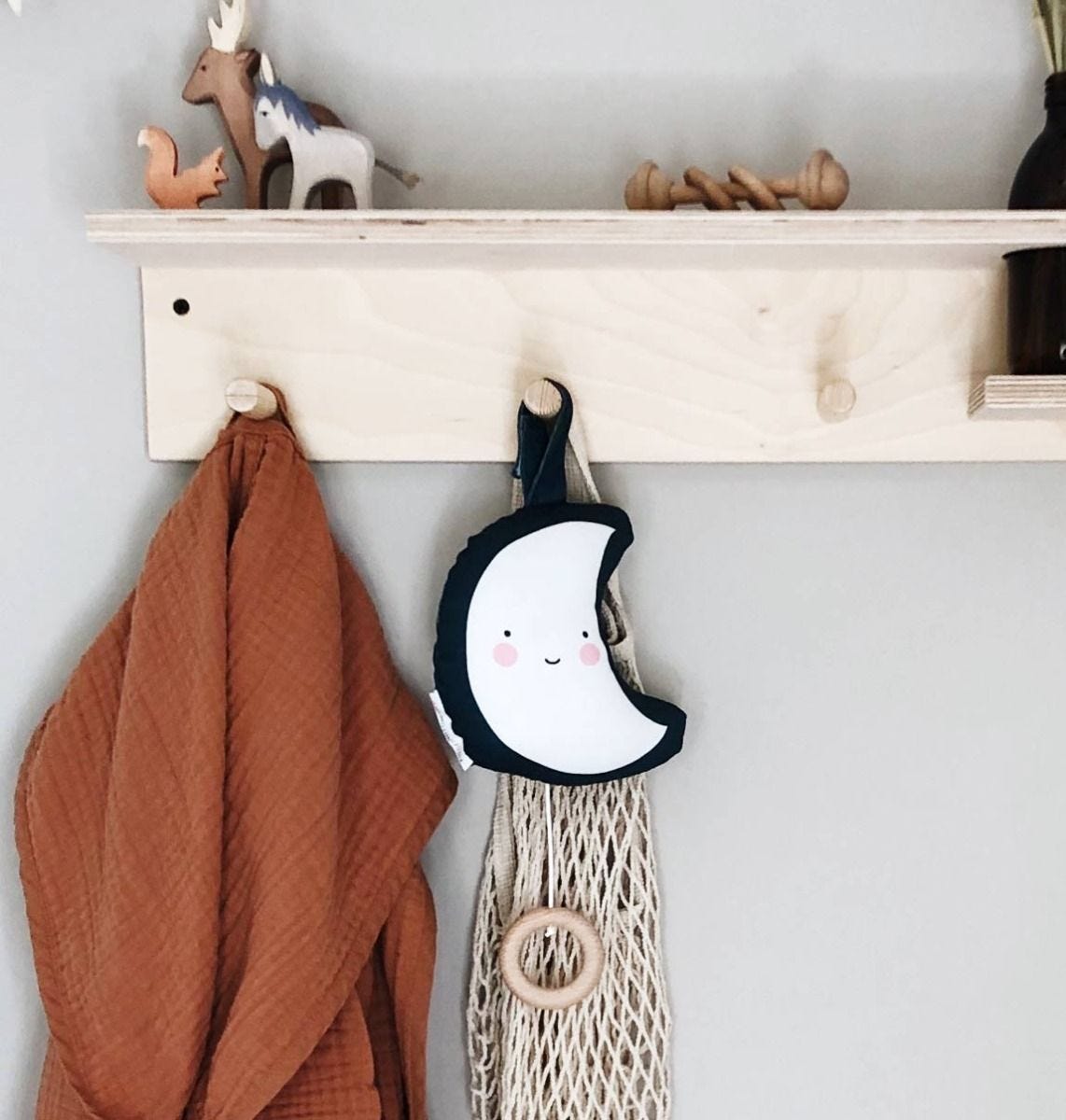 Cabide de parede com casaco castanho, rede com argola e almofada de meia-lua sorridente