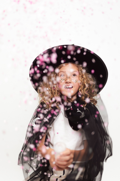 Criança vestida com capa e chapéu pretos com confetes a cair